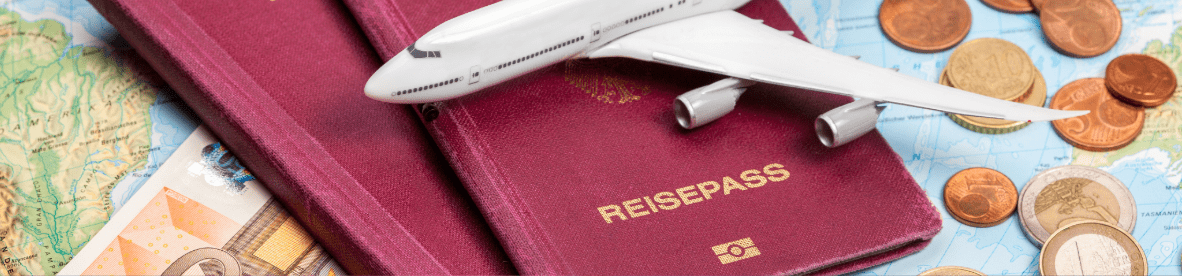 Ein Modell eines weißen Passagierflugzeugs liegt auf zwei roten Reisepässen mit der Aufschrift „REISEPASS“. Im Hintergrund sind eine Landkarte sowie verschiedene Euro-Münzen und -Geldscheine zu sehen.